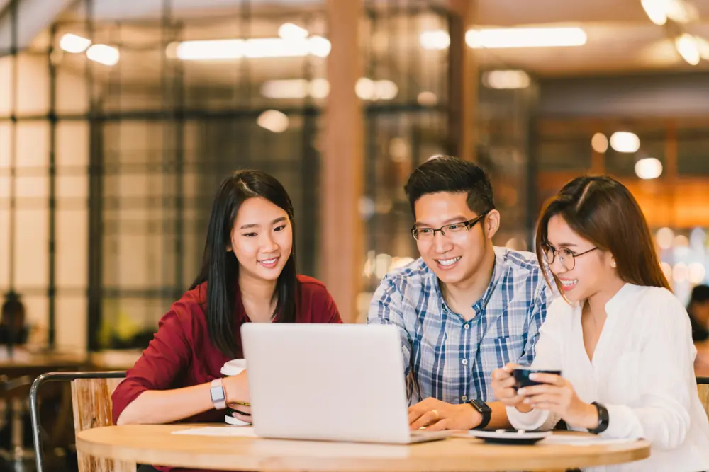 Understanding TOCFL: The Test of Chinese as a Foreign Language 1 Three people are gathered around a laptop in a cafe, studying for the TOCFL exam, with coffee cups on the table signaling a casual yet focused atmosphere.