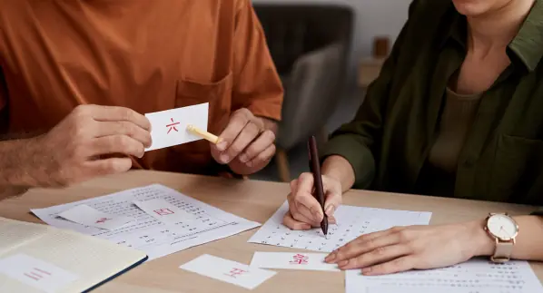 Understanding TOCFL: The Test of Chinese as a Foreign Language 2 A student practices Chinese characters for the TOCFL exam, with a tutor showing a flashcard.