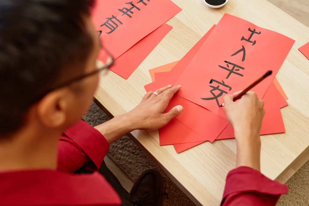 High angle closeup of Asian man writing hieroglyphs with ink and brush doing traditional Chinese calligraphy for New Years day
