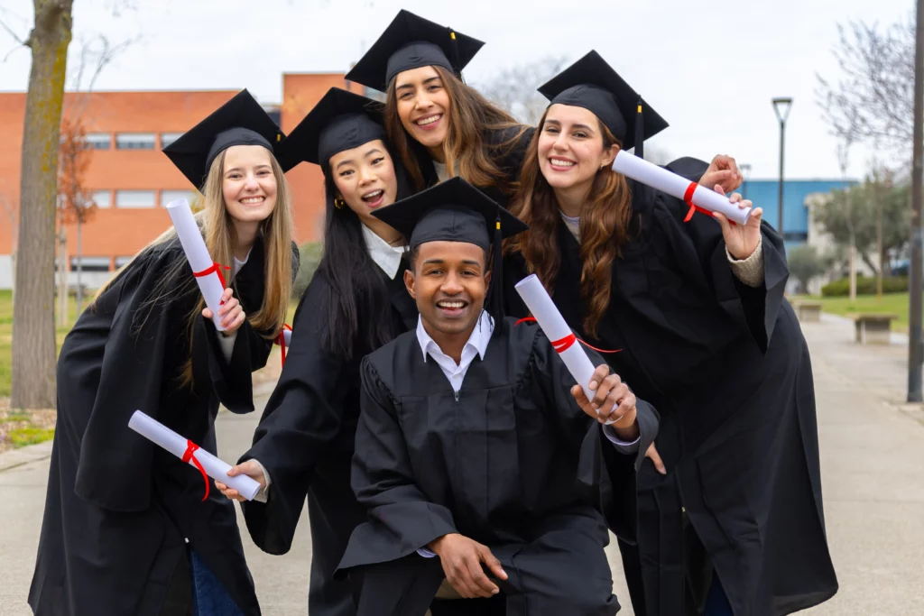 Smiling college students wearing graduation gowns and holding their diplomas.